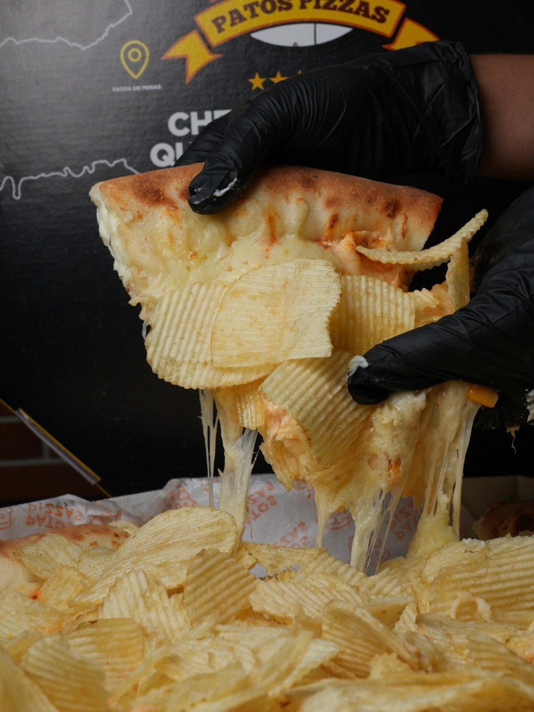 Fatia de pizza de batata sendo puxada com luvas pretas